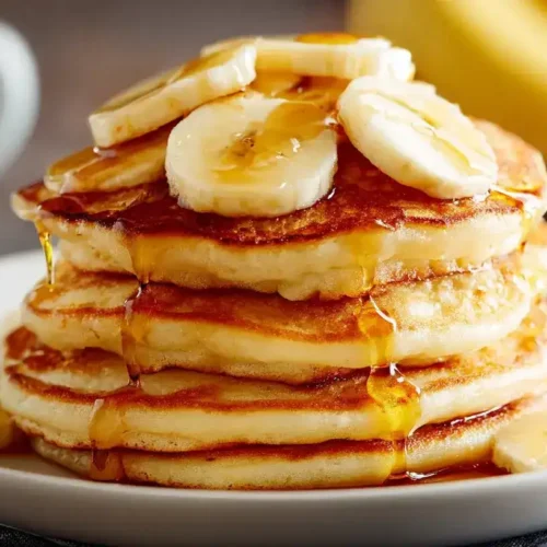 Frisch gebackene Bananen-Pancakes auf Teller mit Bananenscheiben und Ahornsirup